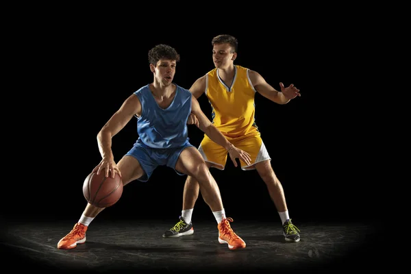 Competitive sport. Two male athletes, professional basketball players in action, motion isolated over black background.