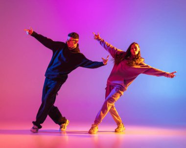 Gündelik kıyafetlerle dans eden iki genç adam ve kız pembe arka planda neon ışıkta hip-hop yapıyorlar..