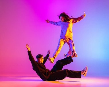 Gündelik kıyafetlerle dans eden iki genç adam ve kız pembe arka planda neon ışıkta hip-hop yapıyorlar..