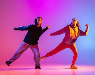 Gündelik kıyafetlerle dans eden iki genç adam ve kız pembe arka planda neon ışıkta hip-hop yapıyorlar..