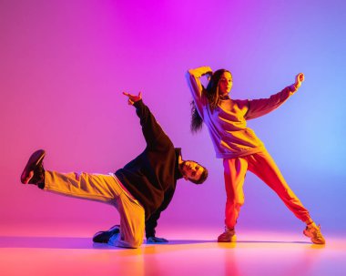 Gündelik kıyafetlerle dans eden iki genç adam ve kız pembe arka planda neon ışıkta hip-hop yapıyorlar..