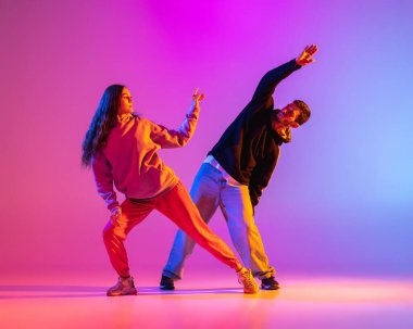 Gündelik kıyafetlerle dans eden iki genç adam ve kız pembe arka planda neon ışıkta hip-hop yapıyorlar..