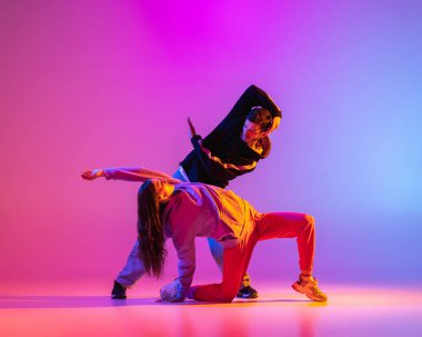 Gündelik kıyafetlerle dans eden iki genç adam ve kız pembe arka planda neon ışıkta hip-hop yapıyorlar..