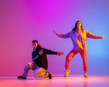 Gündelik kıyafetlerle dans eden iki genç adam ve kız pembe arka planda neon ışıkta hip-hop yapıyorlar..