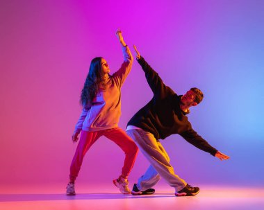 Gündelik kıyafetlerle dans eden iki genç adam ve kız pembe arka planda neon ışıkta hip-hop yapıyorlar..