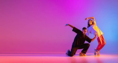 Gündelik kıyafetlerle dans eden iki genç adam ve kız pembe arka planda neon ışıkta hip-hop yapıyorlar..