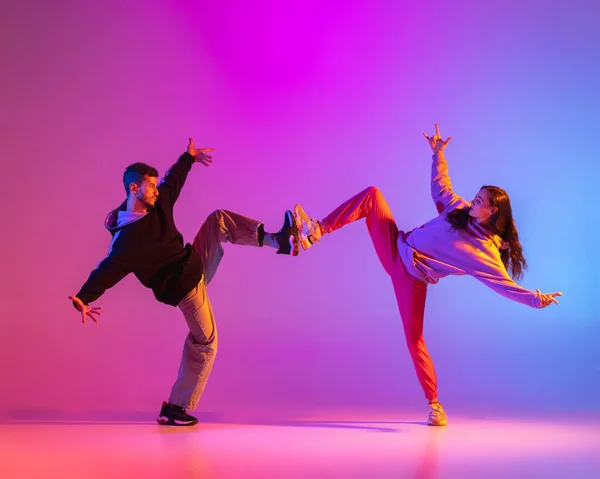 Dos jóvenes, chico y chica en ropa casual bailando danza contemporánea, hip-hop sobre fondo rosa en luz de neón. — Foto de Stock