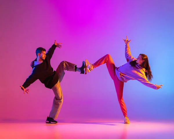 Due giovani, ragazzo e ragazza in abiti casual ballare danza contemporanea, hip-hop su sfondo rosa in luce al neon. — Foto Stock