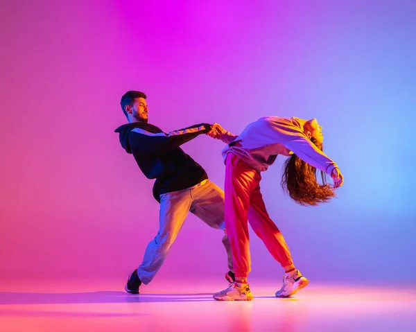 Due giovani, ragazzo e ragazza in abiti casual ballare danza contemporanea, hip-hop su sfondo rosa in luce al neon. — Foto Stock