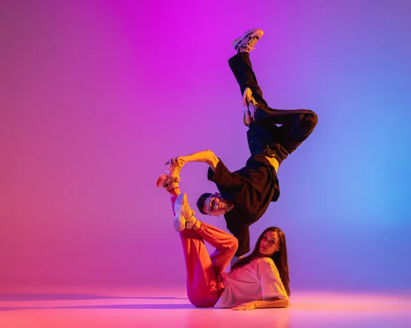 Due giovani, ragazzo e ragazza in abiti casual ballare danza contemporanea, hip-hop su sfondo rosa in luce al neon. — Foto Stock