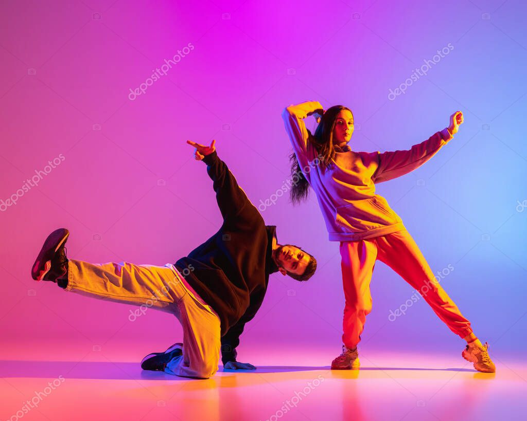 Dos jovenes chico y chica en ropa casual bailando danza contemporanea hip hop sobre fondo rosa en luz de neon. Foto de stock LustreArt 497207890
