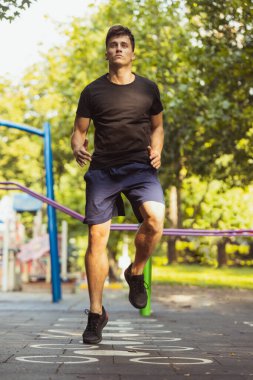 Spor giyim antrenmanında genç, yakışıklı beyaz bir adam açık havada spor yapıyor..