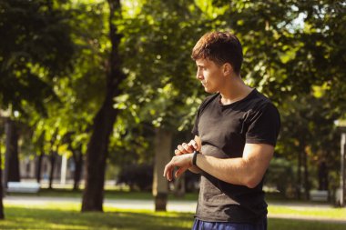 Beyazlı genç bir adam, nabız ölçen bir atlet, spor sahasındaki eğitimden sonra kalp atışları bilezik takıyor..