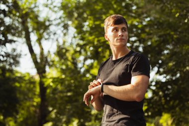 Beyazlı genç bir adam, nabız ölçen bir atlet, spor sahasındaki eğitimden sonra kalp atışları bilezik takıyor..