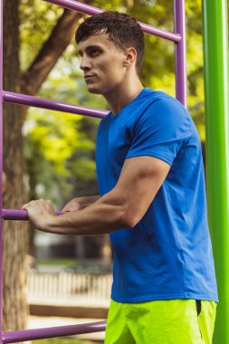 Genç, yakışıklı, beyaz bir adam açık hava spor sahasında güneşli bir yaz gününde dinleniyor..