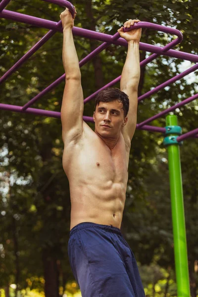 Un joven guapo hombre caucásico en entrenamiento de ropa deportiva, haciendo ejercicio en el campo de deportes al aire libre en el día de verano brillante. —  Fotos de Stock