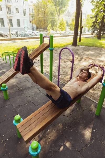 Ein junger gutaussehender kaukasischer Mann in Sportkleidung trainiert an einem strahlenden Sommertag auf einem Sportplatz im Freien. — Stockfoto
