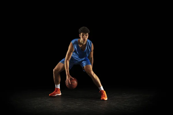 En ung kaukasiska professionell basketspelare tränar med bollen isolerad på svart bakgrund — Stockfoto