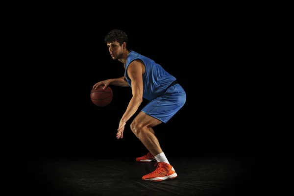Sidovy. En ung kaukasiska professionell basketspelare tränar med bollen isolerad på svart bakgrund — Stockfoto