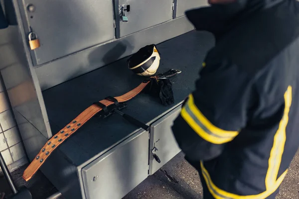 Un bombero masculino vestido de uniforme con casco protector en la estación de bomberos. Vista trasera —  Fotos de Stock