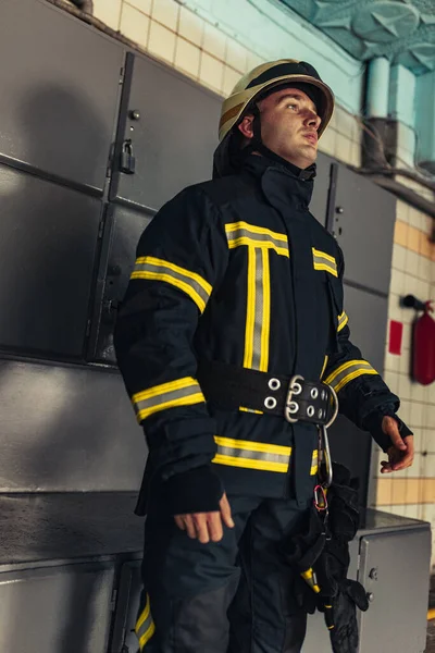 Un bombero masculino vestido de uniforme con casco protector en la estación de bomberos —  Fotos de Stock