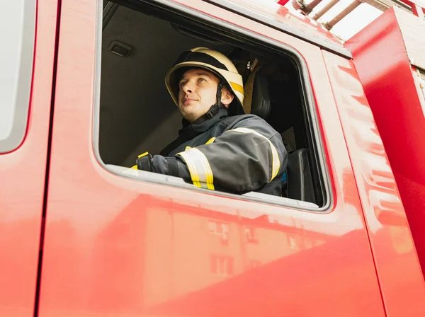 Один молодий чоловік пожежник одягнений в уніформу з захисним шоломом у пожежній машині . — стокове фото