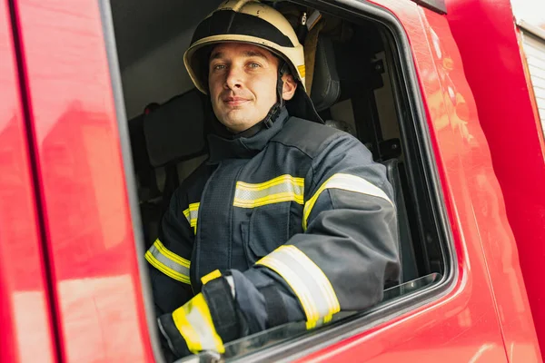 One young male firefighter dressed in uniform with protective helmet in fire truck.