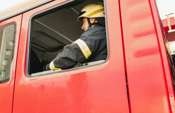 Jeden młody strażak ubrany w mundur w hełm ochronny w wozie strażackim. — Zdjęcie stockowe