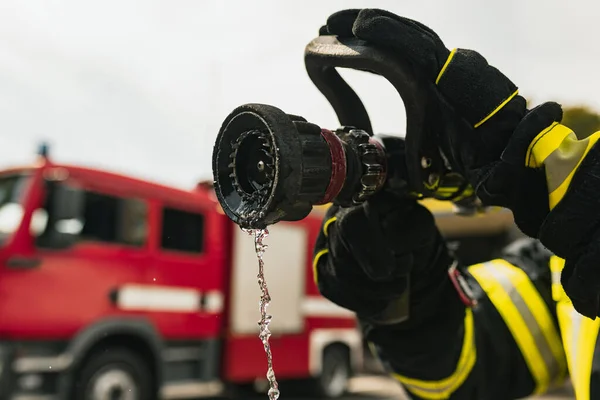 Bombero en servicio con manguera de agua en frente de camión de bomberos listo para extinguir. Primer plano —  Fotos de Stock