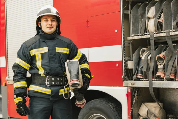 Один молодий чоловік пожежник, одягнений в уніформу з водяним шлангом на пожежній машині, готовий до розгортання — стокове фото