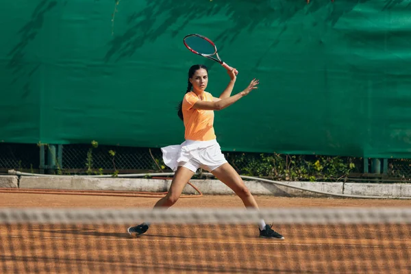 En vacker ung idrottskvinna, professionell tennisspelare med racket tränar på lera tennisbana i sommar dag. — Stockfoto