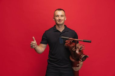 Kırmızı arka planda duran itfaiye vanası ile gülümseyen genç adamın portresi.