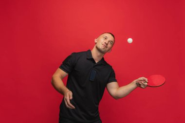 Beyaz tenli genç bir adam masa tenisi oynuyor. Kırmızı arka planda..