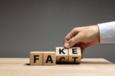 Erkek el, tahta küpleri, gri arka plandaki ahşap masada sahte sözlerle çevirir. Reklam için kopyalama alanı.