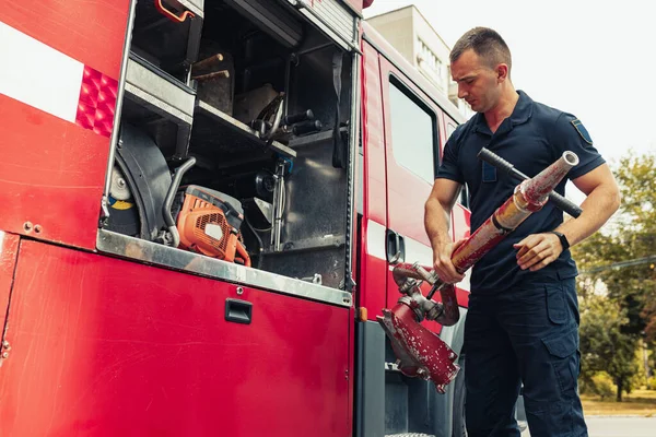 Пожежник стоїть біля пожежної машини, тримаючи пожежний гідрант для аварійної пожежі — стокове фото