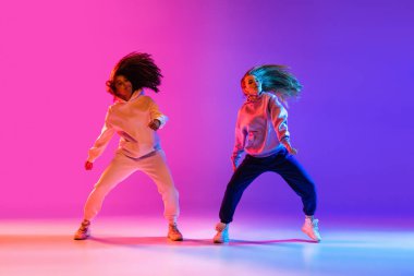 Gradyan pembe neon stüdyo arka planında dans eden iki güzel aktif kız