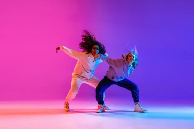İki güzel aktif hip-hop kızı gradyan pembe neon stüdyosunda dans ediyor.