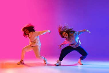 Gradyan pembe neon stüdyo arka planında dans eden iki güzel aktif kız