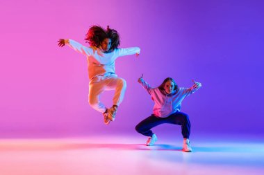 Gradyan pembe neon stüdyo arka planında hip-hop dansı yapan iki güzel genç kız.