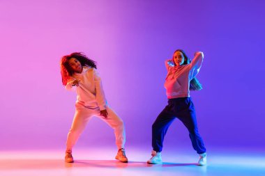 İki güzel genç kız neon renkli arka planda hip-hop dansı yapıyor..