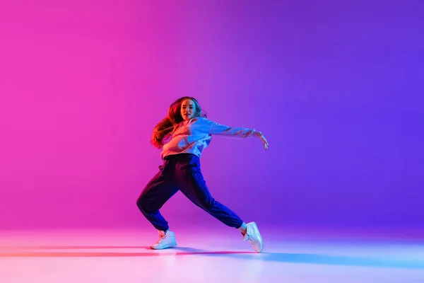 Giovane ragazza attraente, ballerina hip-hop femminile isolato sul gradiente rosa viola neon studio sfondo — Foto Stock