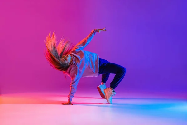 Atractiva joven activa bailando y mostrando trucos de hip-hop aislados en degradado rosa púrpura estudio de neón fondo — Foto de Stock