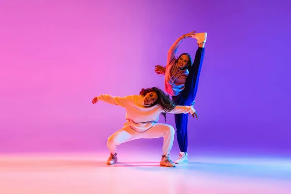 Due belle ragazze che ballano hip-hop sul gradiente rosa viola neon studio sfondo — Foto Stock
