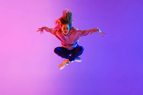 En salto. Joven chica hermosa, bailarina de hip-hop femenina aislada en el fondo del estudio de neón rosa degradado — Foto de Stock