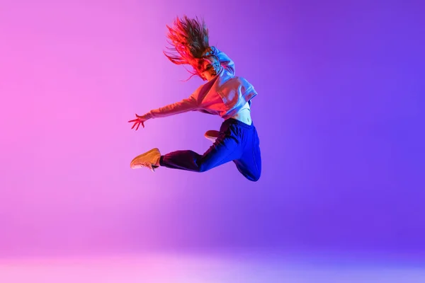 In een sprong. jong stijlvol meisje dansen hip-hop geïsoleerd op gradiënt roze paars neon studio achtergrond — Stockfoto
