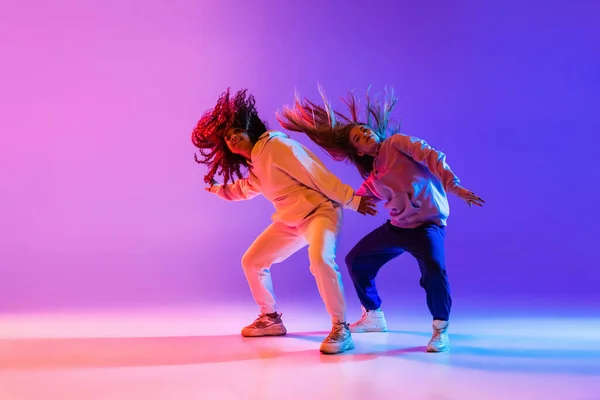 Δύο όμορφες ενεργές κοπέλες χορεύουν σε ροζ μωβ νέον φόντο στούντιο — Φωτογραφία Αρχείου