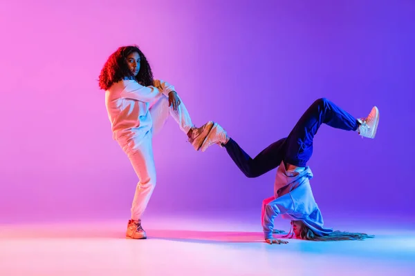 Due belle ragazze che ballano dinamicamente hip-hop su sfondo sfumato colorato al neon. — Foto Stock