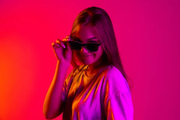 Обрізана стильна молода біла дівчина в чорних модних сонцезахисних окулярах ізольована на неоновому фоні — стокове фото