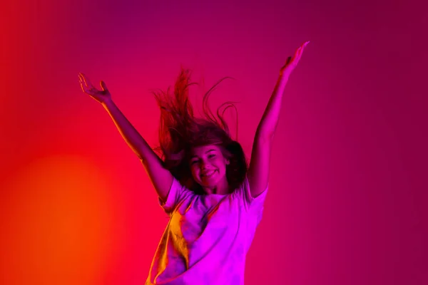 Teljes hosszúságú portré fiatal, gyönyörű lányról mozgásban, feltartott kezekkel, elszigetelve színes sárga rózsaszín vörös háttéren, neonban. — Stock Fotó