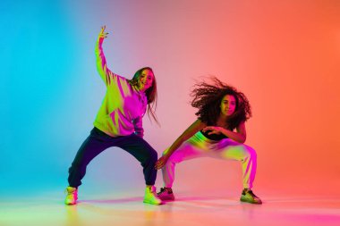 İki güzel kız neon ışıklarıyla renkli arka planda hip-hop yapıyor.